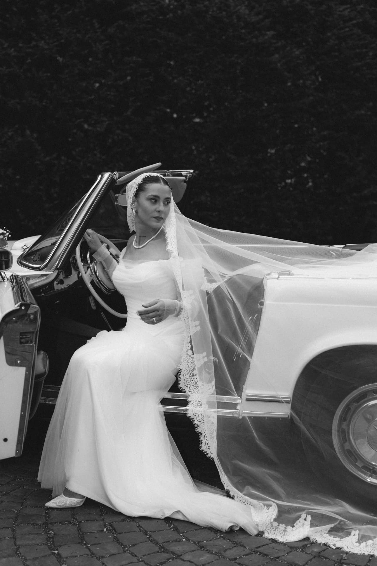 Braut in Schwarzweiß im weißen Mercedes Oldtimer Cabrio – luxuriöse Hochzeitsfotografie