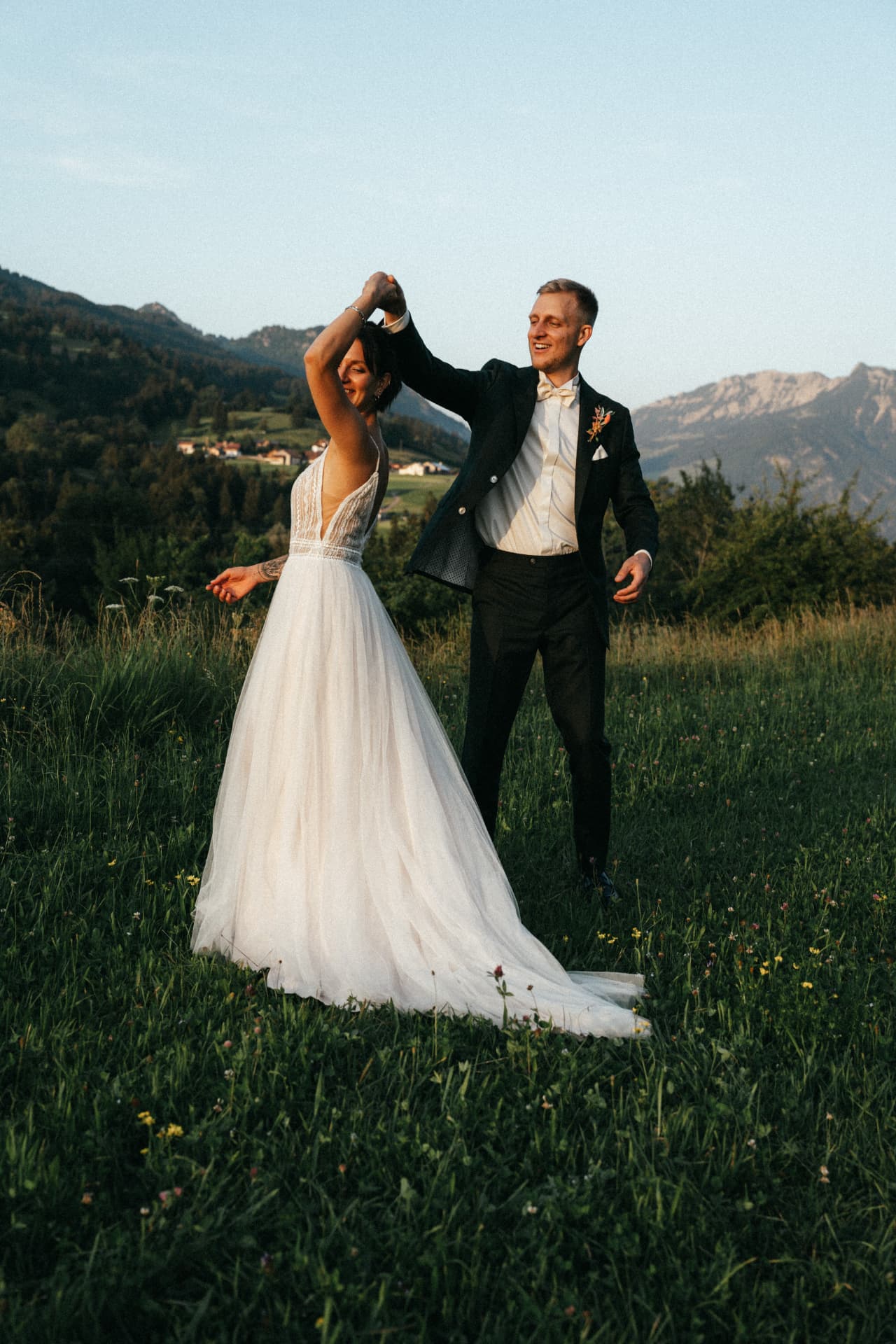 Brautpaar tanzt auf Bergwiese vor Alpenpanorama – emotionale Hochzeitsfotografie