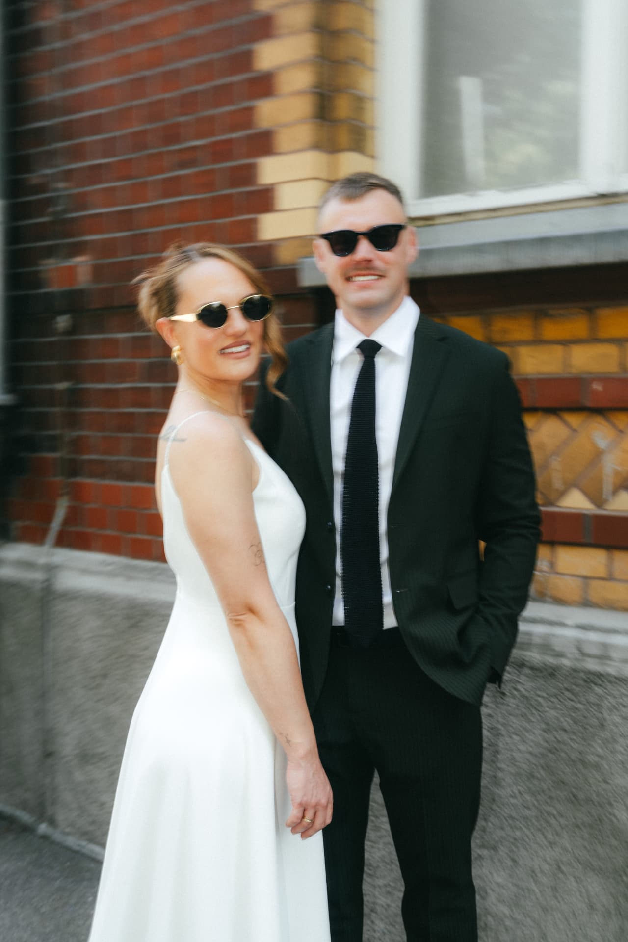 Stylisches Brautpaar mit Sonnenbrillen vor Backsteinfassade – Hochzeitsfotograf Augsburg