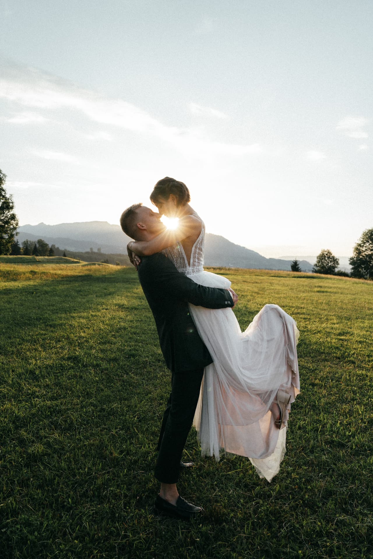 Bräutigam hebt Braut im Gegenlicht auf Bergwiese – Hochzeitsfotograf Allgäu