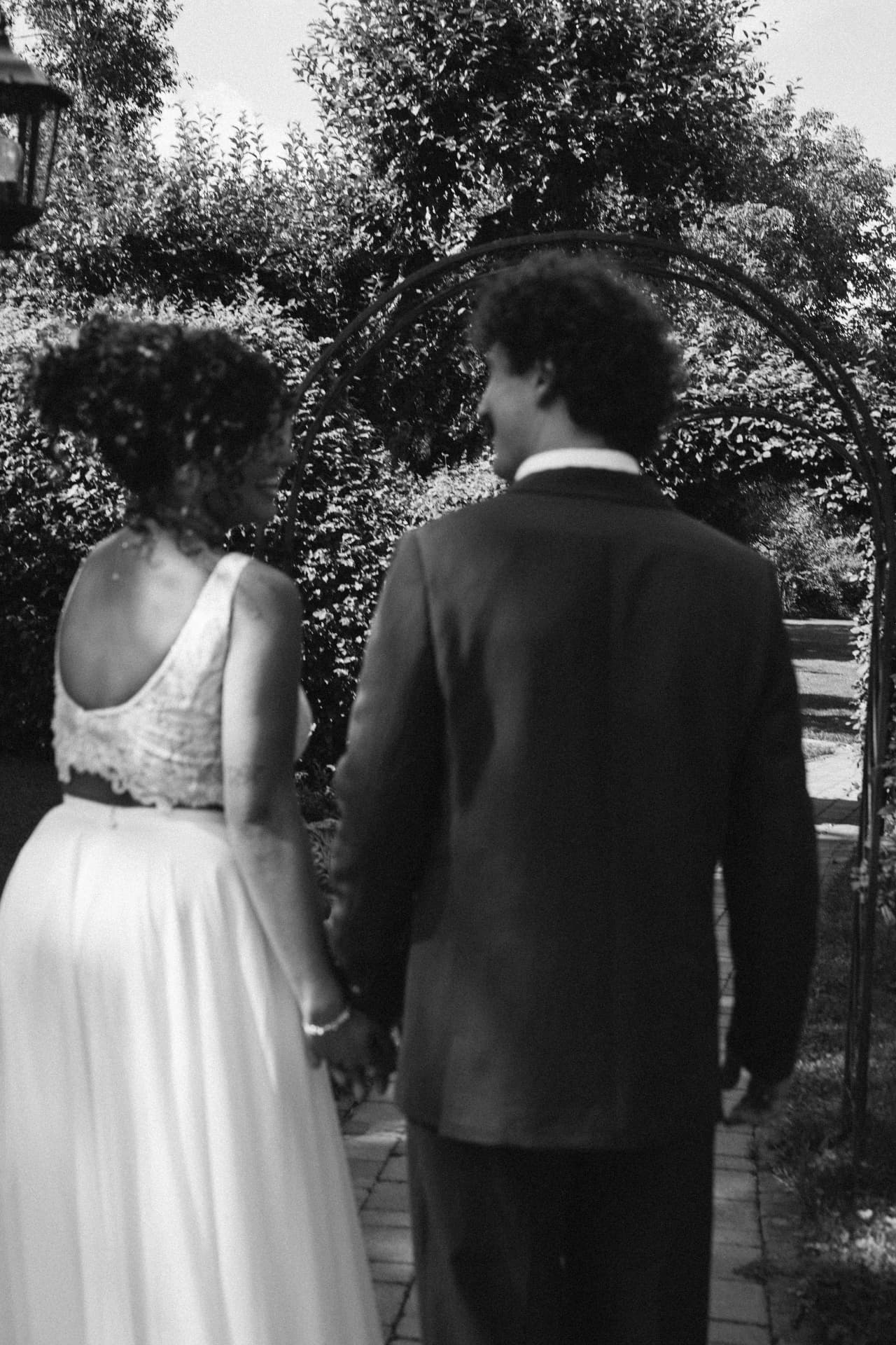Brautpaar Hand in Hand unter Rosenbogen in Schwarzweiß – Hochzeitsfotograf Augsburg