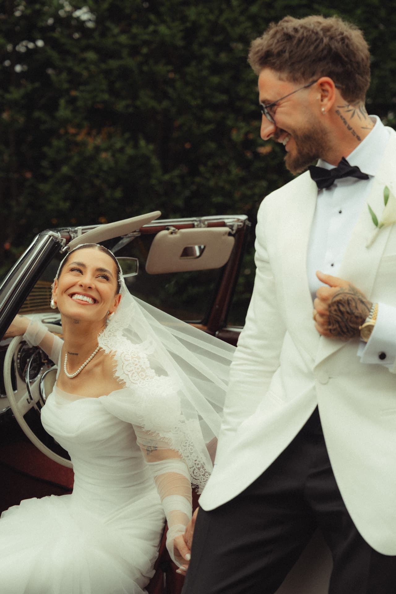 Braut lacht im Oldtimer Cabrio mit Bräutigam im weißen Smoking – luxuriöse Hochzeit