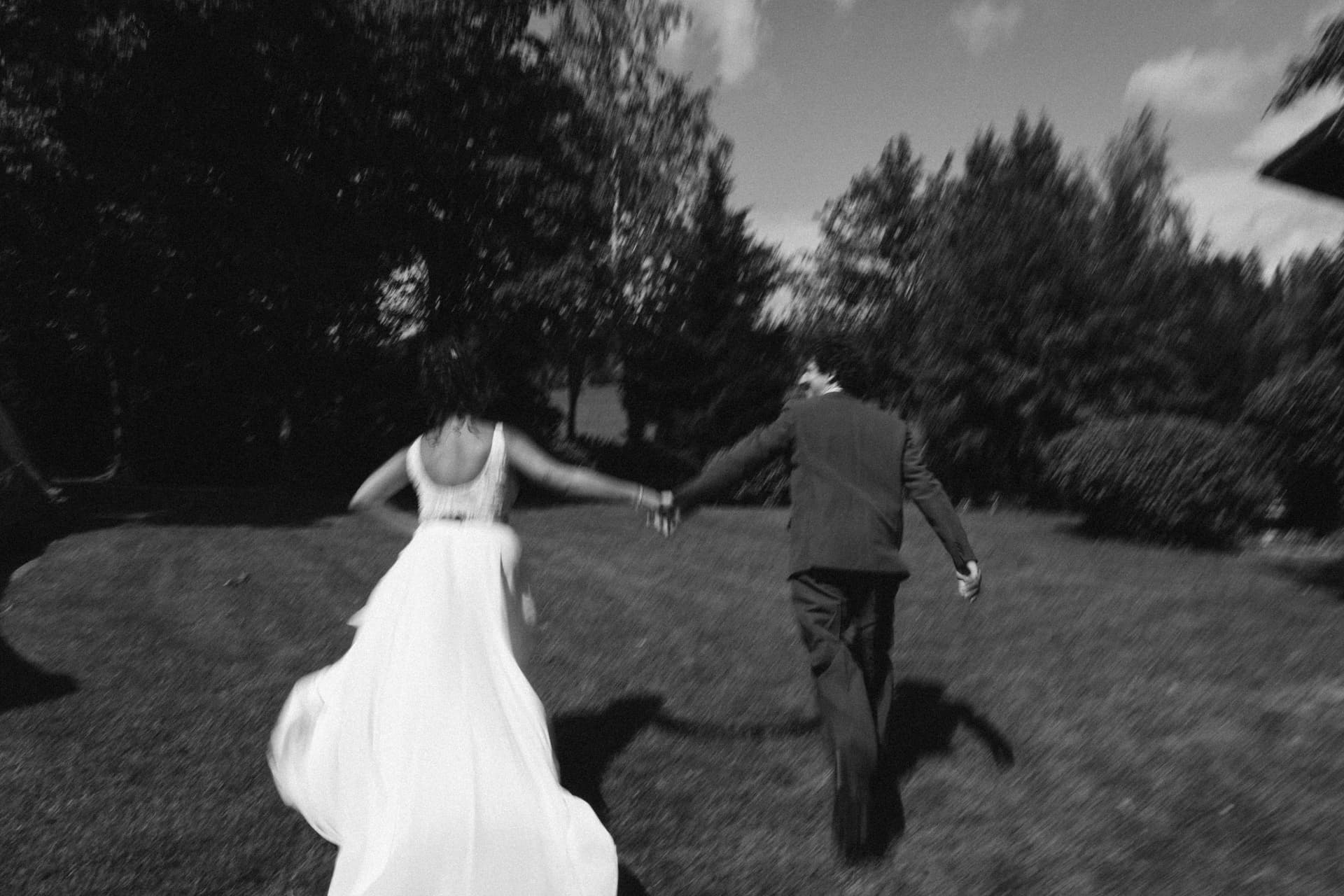 Brautpaar läuft Hand in Hand über Wiese – schwarzweiße Hochzeitsfotografie Augsburg
