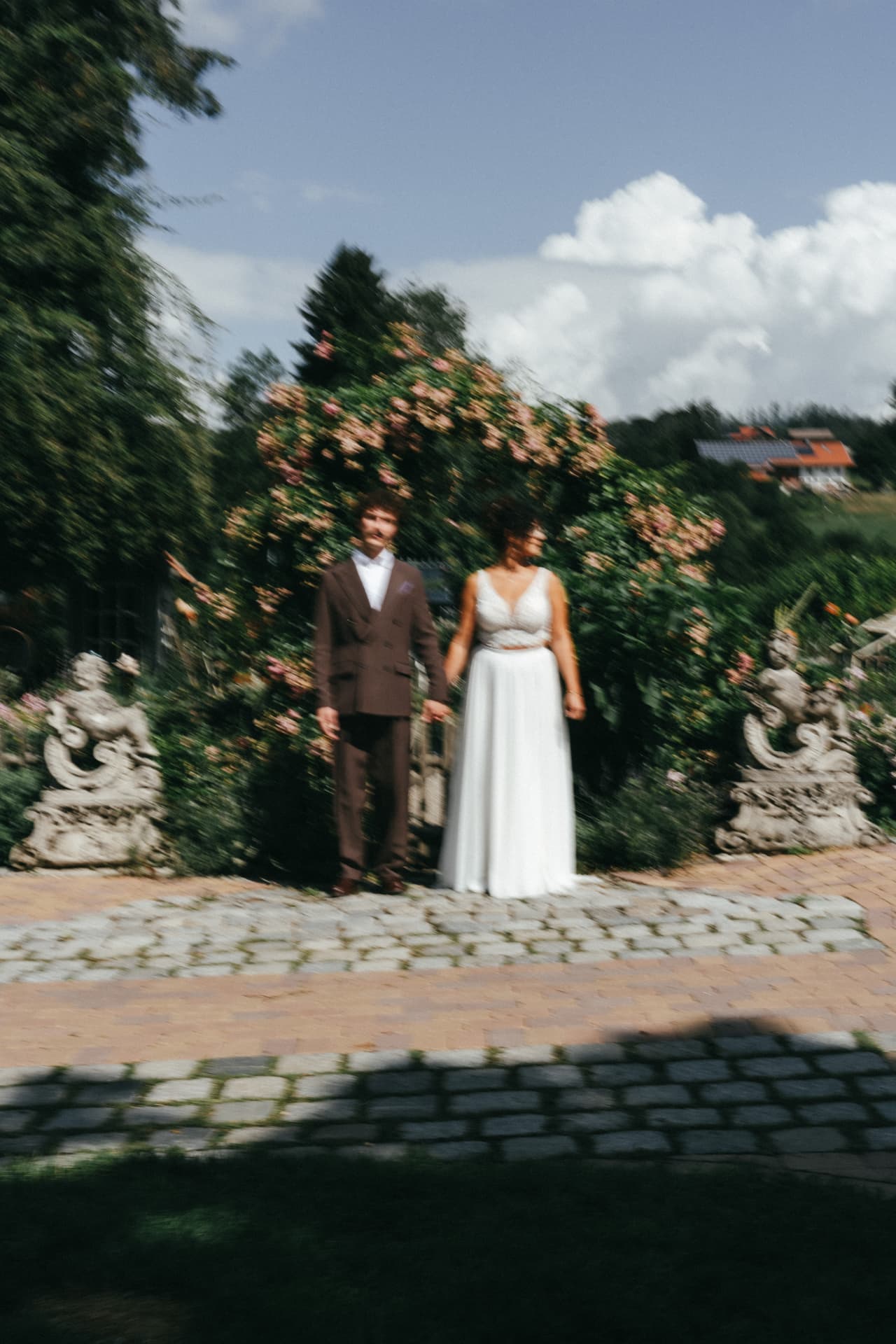 Brautpaar Hand in Hand vor blühendem Rosenbogen – künstlerisch bewegte Hochzeitsfotografie